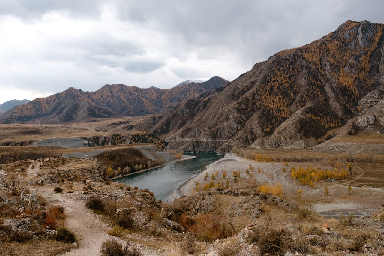 Breathtaking view of a serene river winding through the rugged Siberian mountains under a cloudy sky.