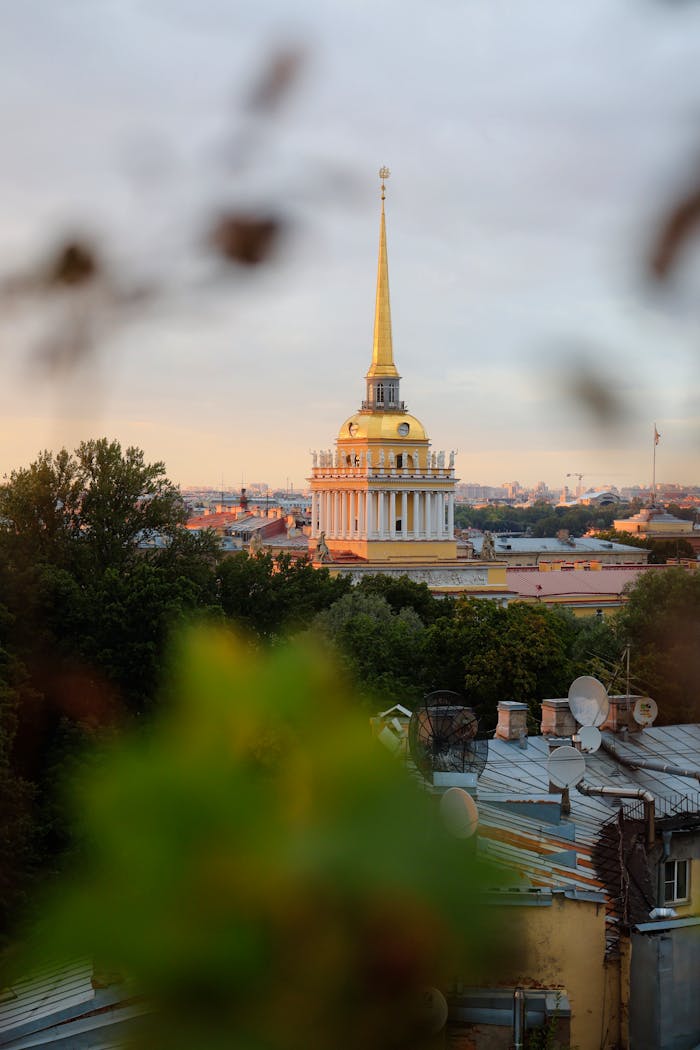 Golden spire of the Admiralty Building amidst Saint Petersburg cityscape at sunset.